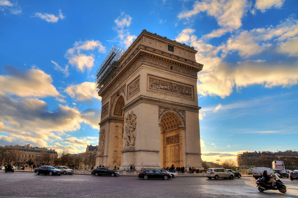 The Arc de Triomphe in Paris with a clear sky and surrounding traffic.