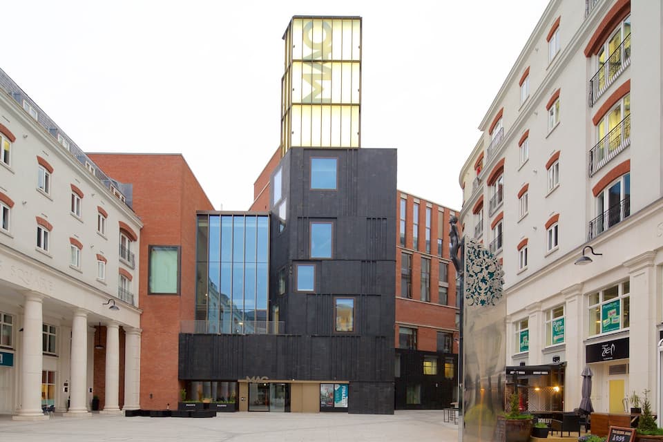 A modern building with a glass facade, surrounded by traditional buildings with red brick facades and white trim.