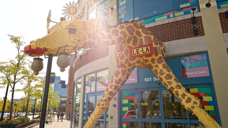 A LEGO giraffe sculpture in front of a building with a 'LEGO' sign.
