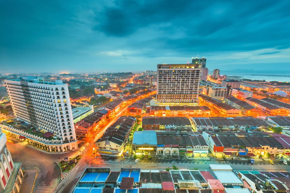 A cityscape at dusk with illuminated buildings and a river in the background.