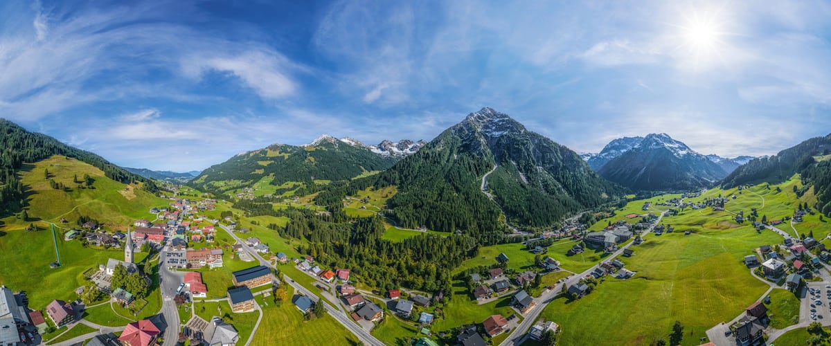 A panoramic view of a mountain village with a prominent church, lush green fields, and a clear sky.