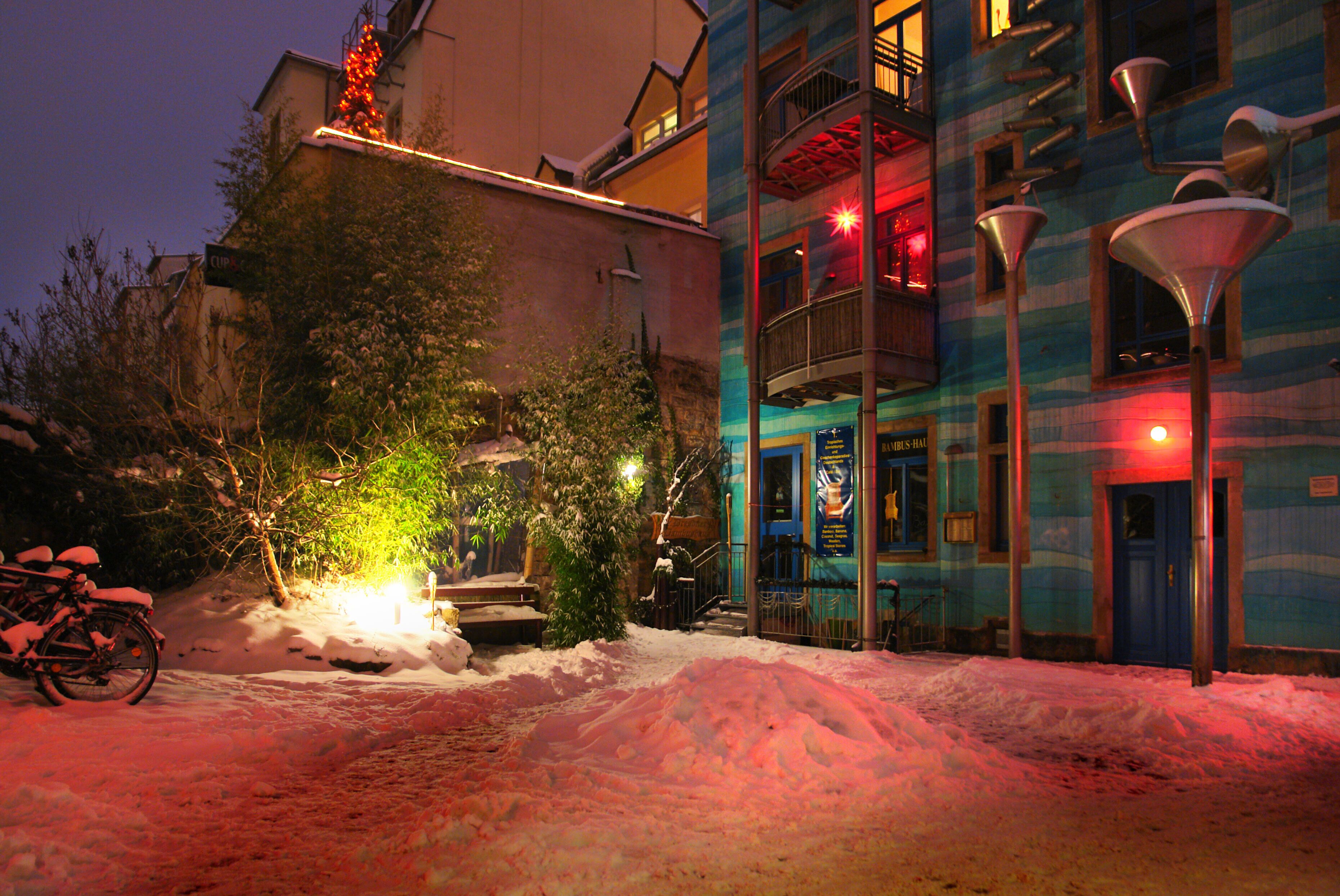 A snow-covered street with a bicycle, a building with balconies, and street lamps.