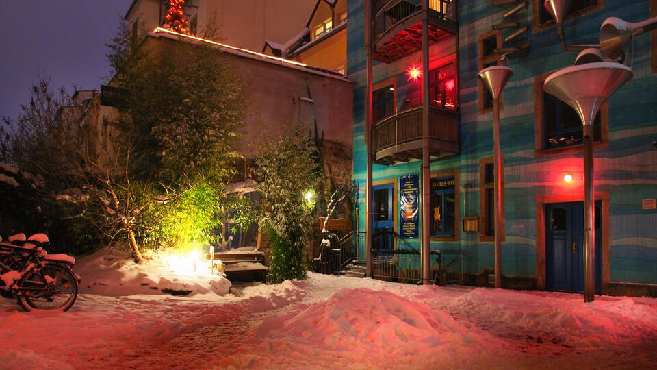 A snow-covered street with a bicycle, a building with balconies, and street lamps.