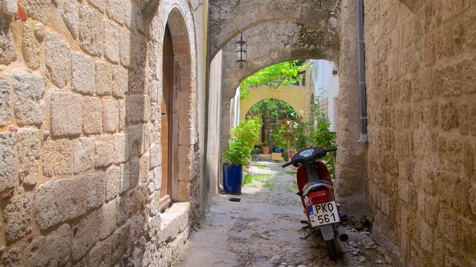 A narrow stone alleyway with a red scooter parked at the end.