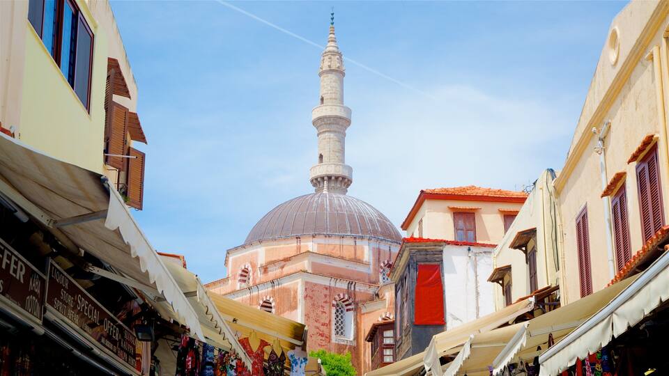 A mosque with a tall minaret and a dome, surrounded by narrow streets with shops.
