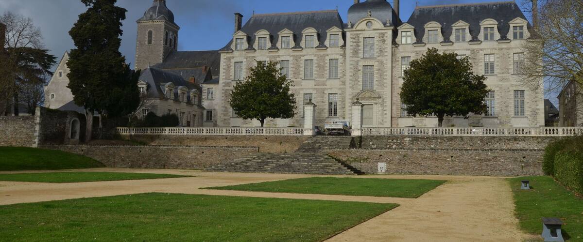 A large historic building with a prominent tower and a well-maintained lawn in front.