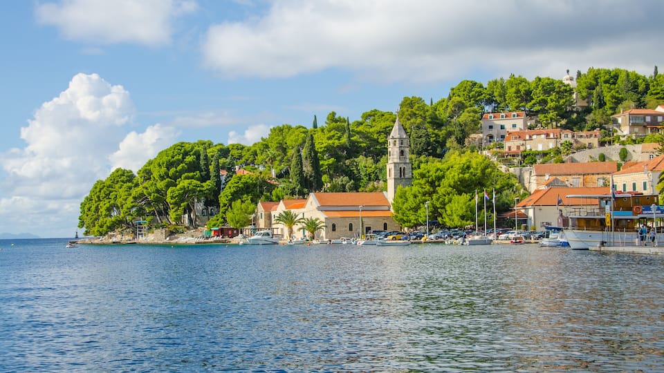 A coastal town with a prominent church on a hill, surrounded by lush greenery and a calm sea.