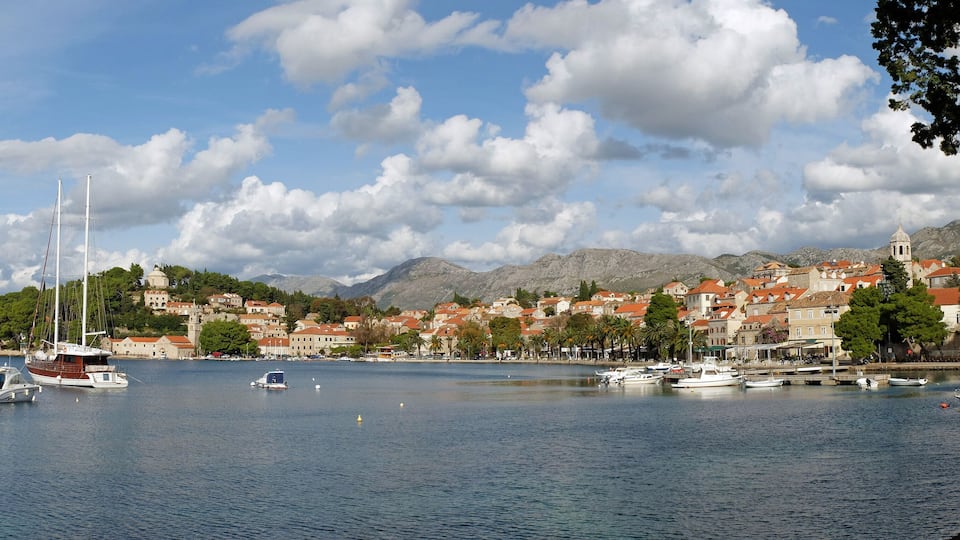 A coastal town with boats on the water, a church, and mountains in the background.