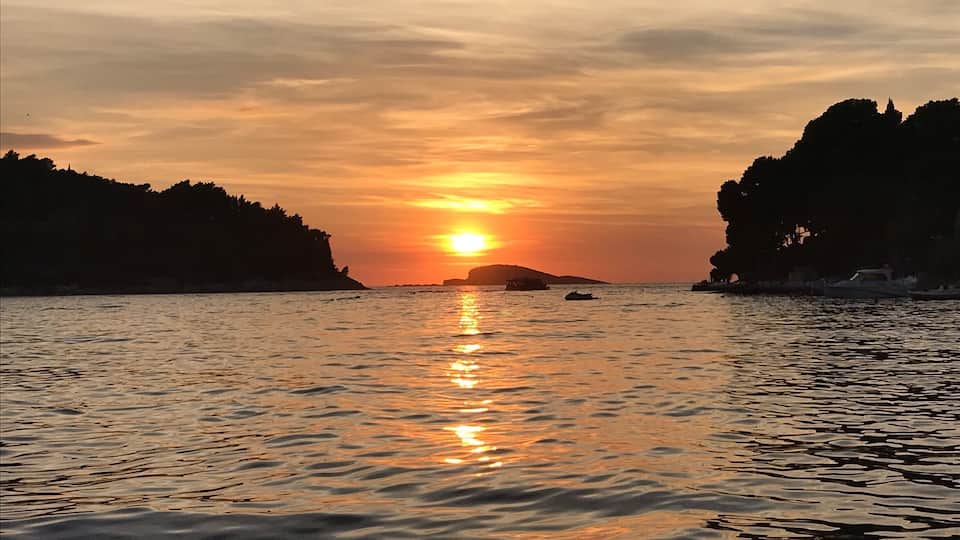A sunset over a calm sea with rocky cliffs on either side.