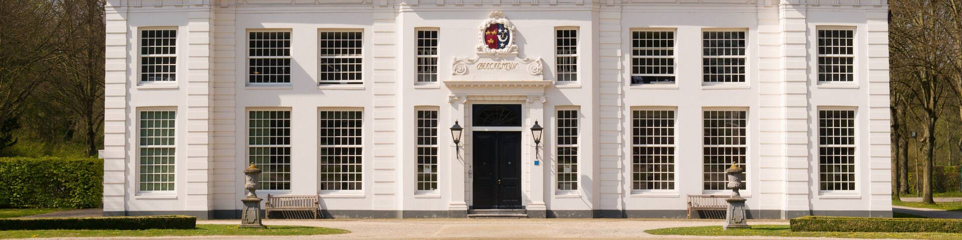 A stately white building with a black roof, a central entrance, and a coat of arms above the door.