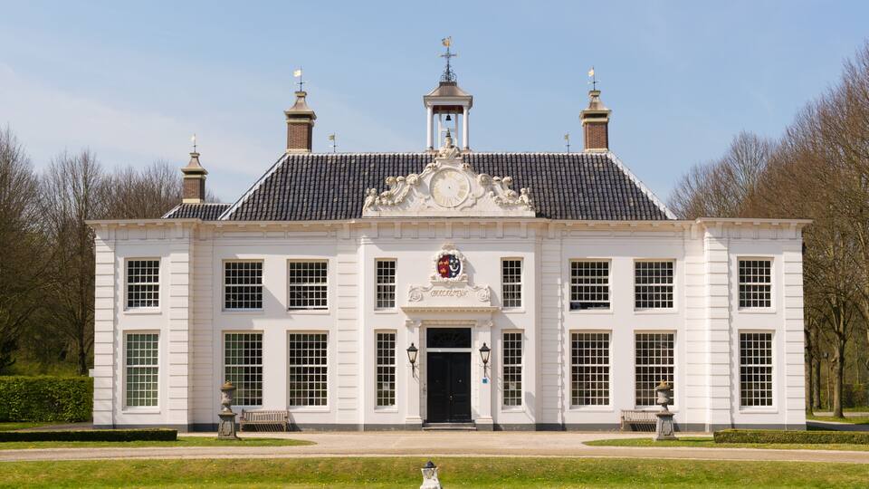 A stately white building with a black roof, a central entrance, and a coat of arms above the door.