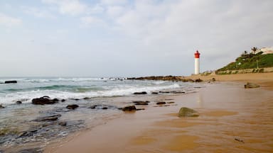 Une plage avec un phare, une côte rocheuse et des vagues qui déferlent sur le sable.