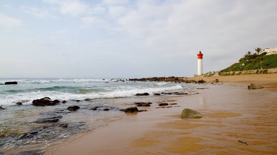 A beach with a lighthouse, rocky shoreline, and waves crashing onto the sand.