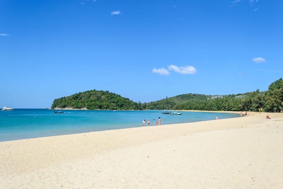 Une plage à l’eau turquoise et limpide, un rivage sablonneux et, au loin, une petite île couverte d’une végétation luxuriante.