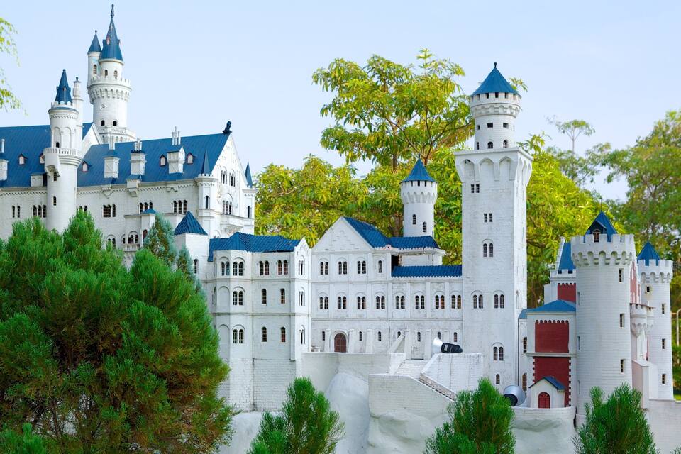 A large white castle with multiple towers and turrets, surrounded by lush green trees.