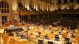 An orchestra in a large hall with high ceilings and columns.