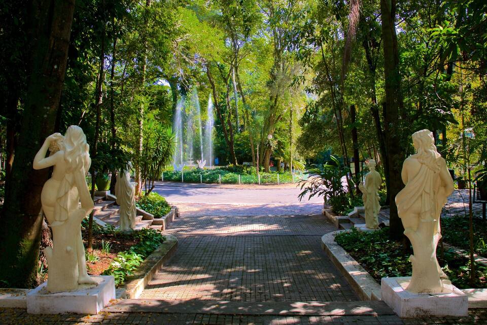 A garden with statues, a fountain, and a paved walkway surrounded by trees.