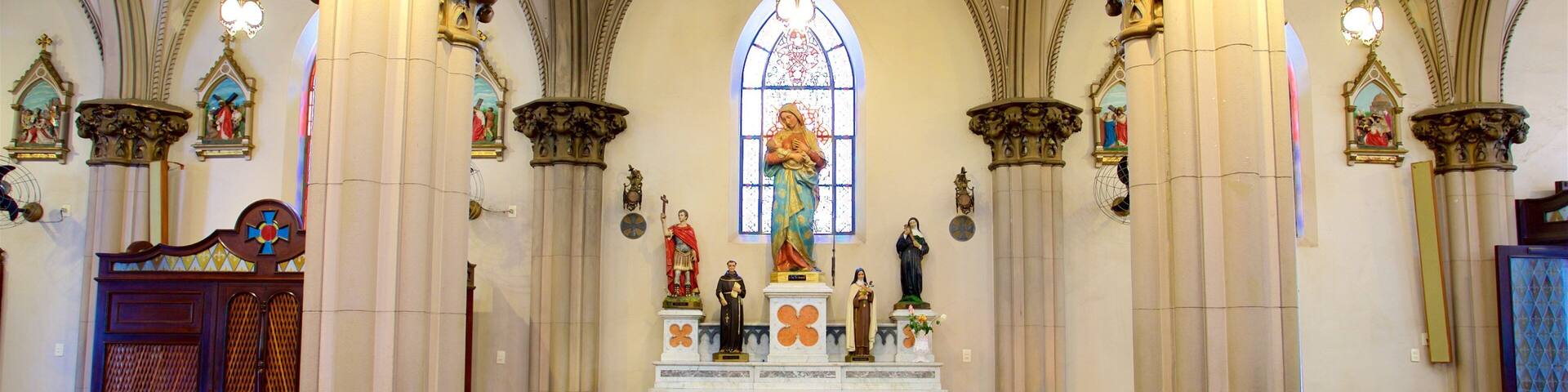 A church interior with high vaulted ceilings, ornate columns, and a central altar with religious statues.