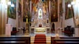 An ornate church interior with a central altar, religious statues, and a large mural on the walls.