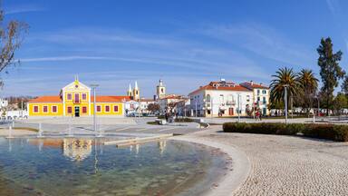 A plaza with a fountain, yellow buildings, and a church with a red roof.