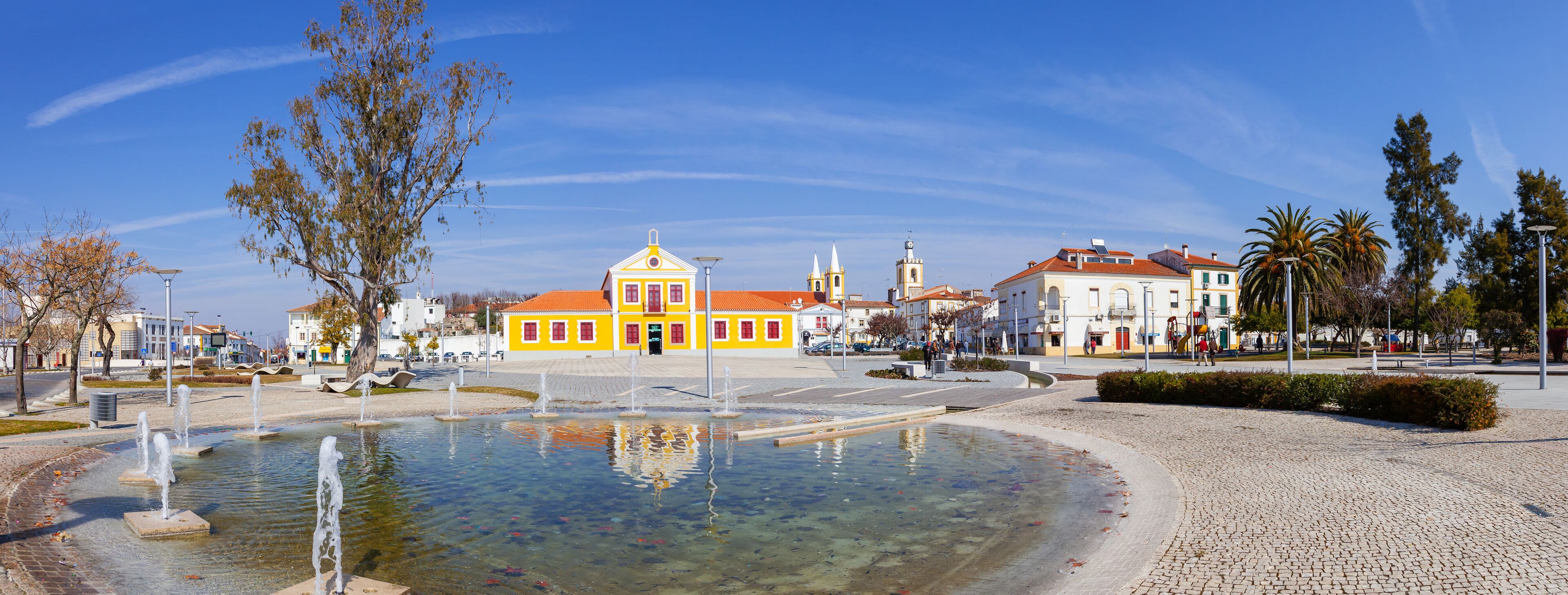 A plaza with a fountain, yellow buildings, and a church with a red roof.