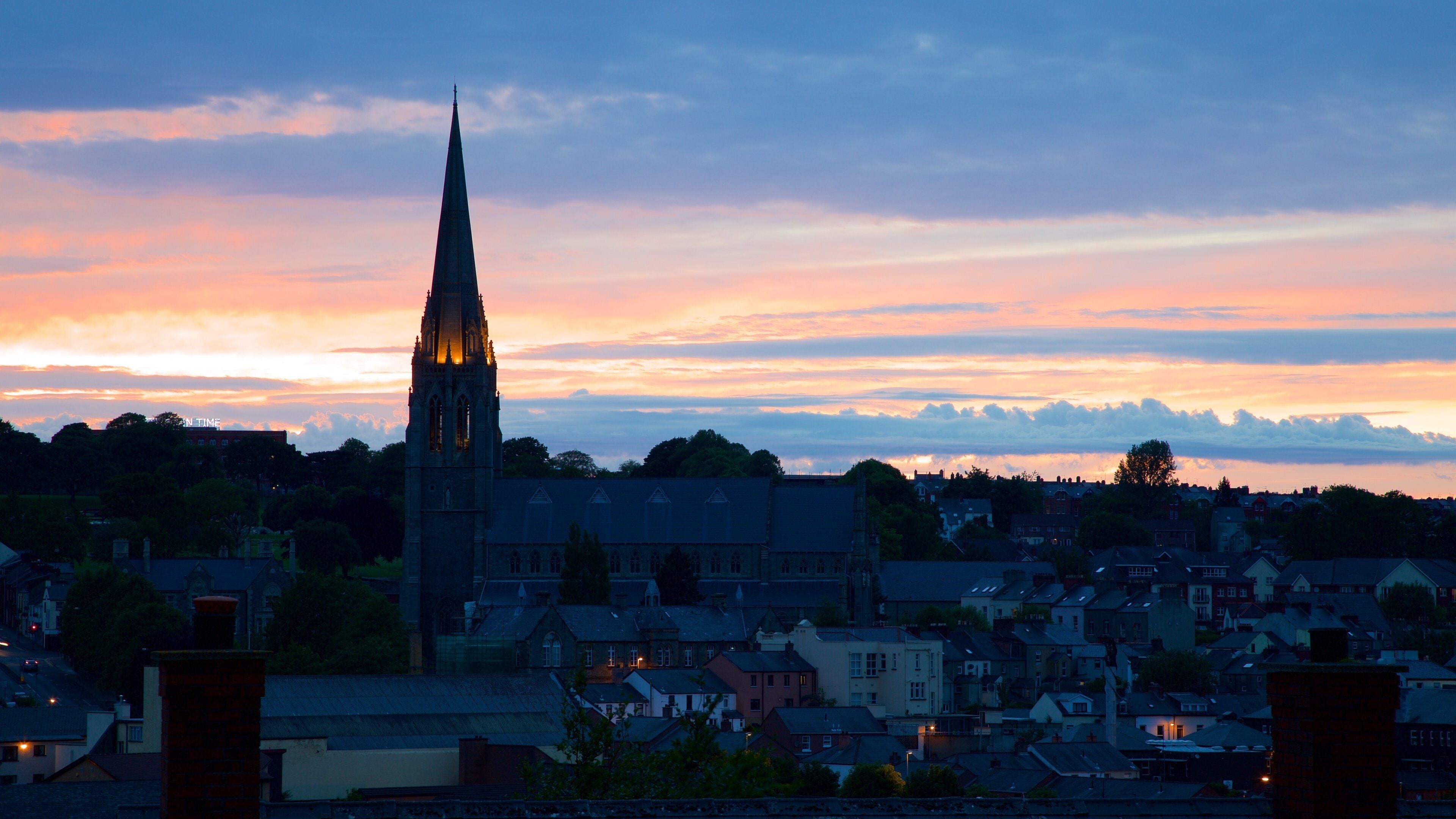 A church with a tall spire, surrounded by residential buildings and a sunset sky.