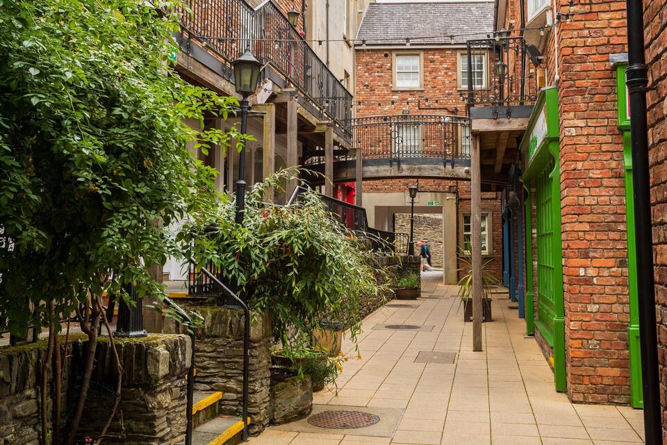 A narrow alley with brick buildings, green shutters, and a stone wall.