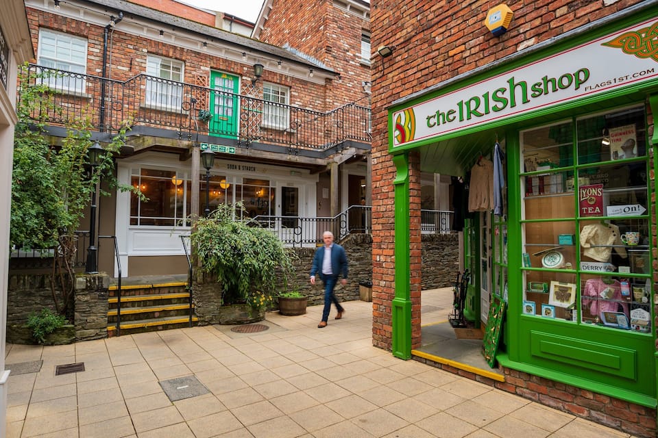 Una calle con un escaparate verde que dice 'The Irish Shop' y un edificio con una puerta verde.