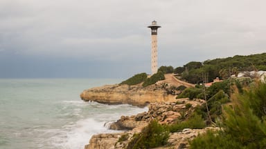 Paisaje costero con un faro en un promontorio rocoso, rodeado de vegetación y un cielo despejado.