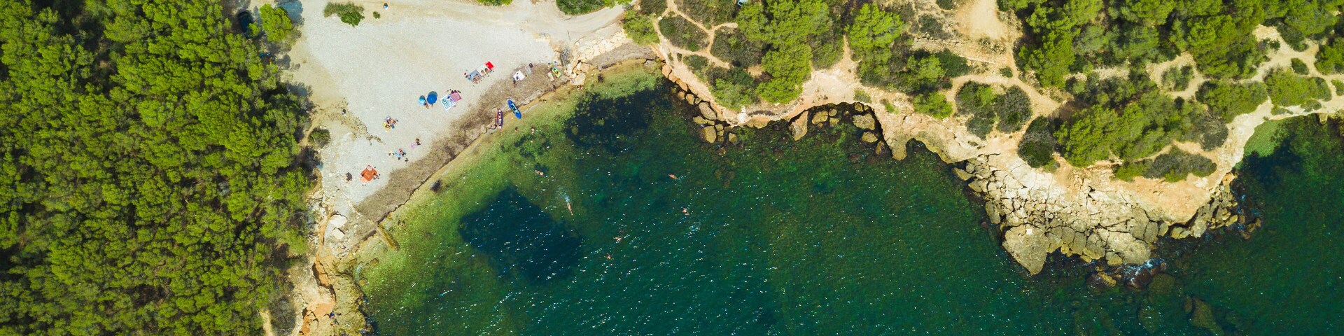 An aerial view of a coastal area with a sandy beach, dense green forest, and a rocky coastline.