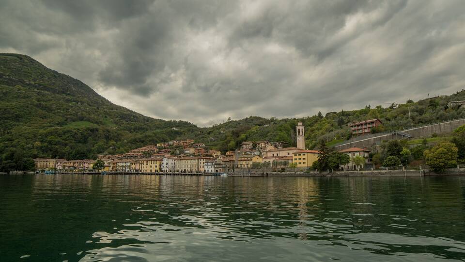 A lakeside town with historic buildings, a prominent tower, and a hillside with dense greenery.