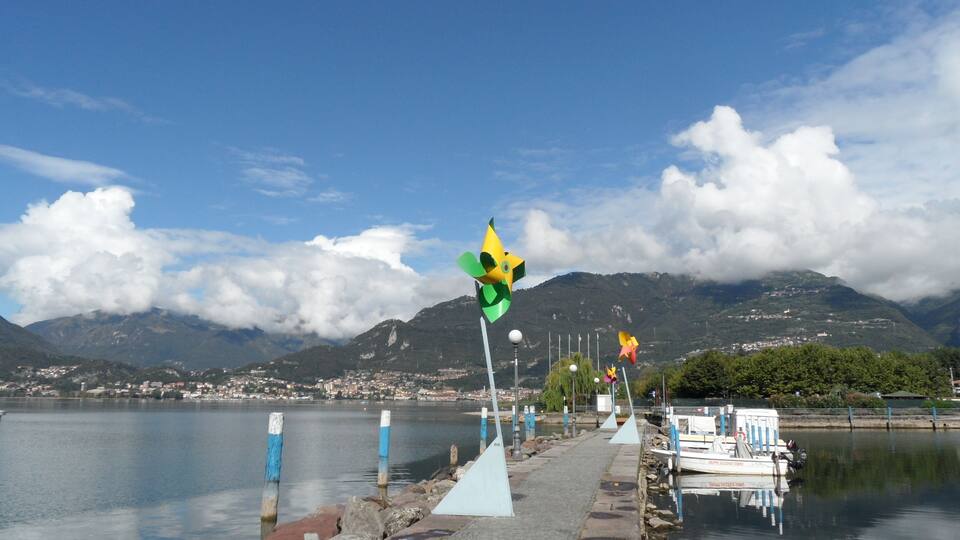 A waterfront with a row of colorful pinwheels, calm water, and a mountainous backdrop.