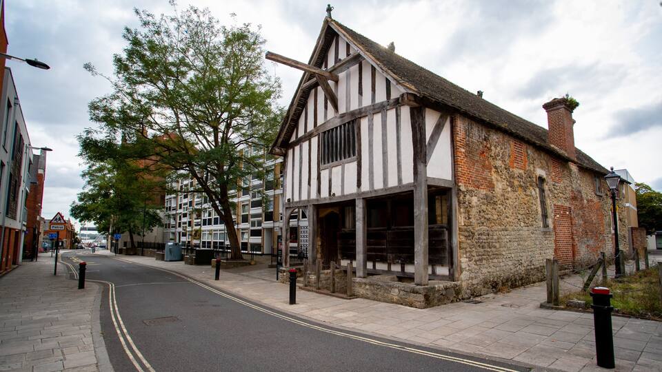 A historic half-timbered building with a cobblestone street and modern buildings in the background.