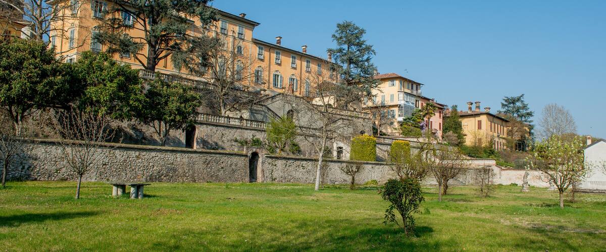 A historic hillside town with terraced buildings, stone walls, and lush greenery.