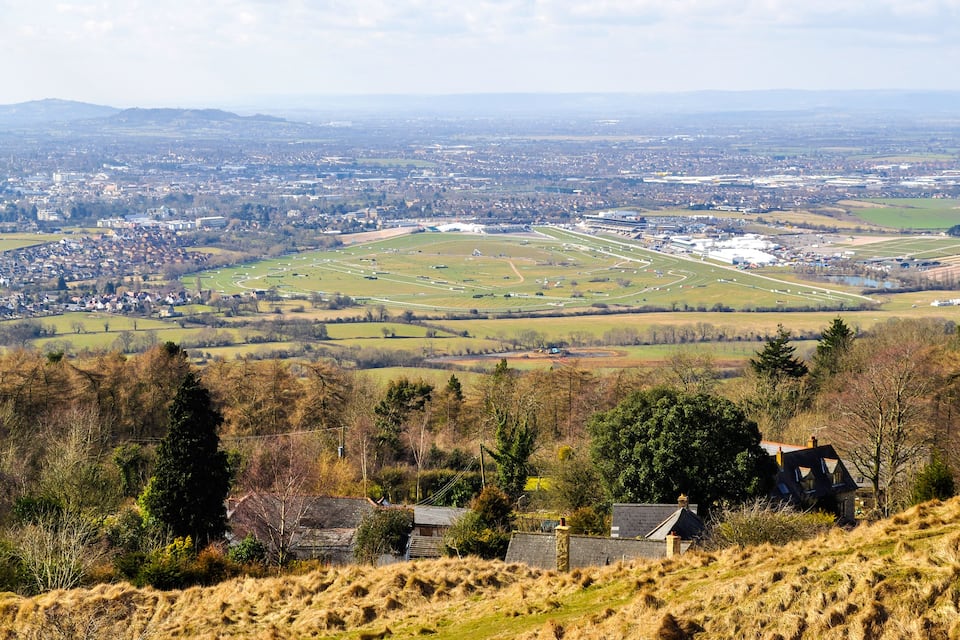 A rural landscape with a large open field, a small village, and distant hills.