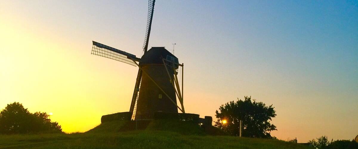 A windmill on a grassy hill during sunset.