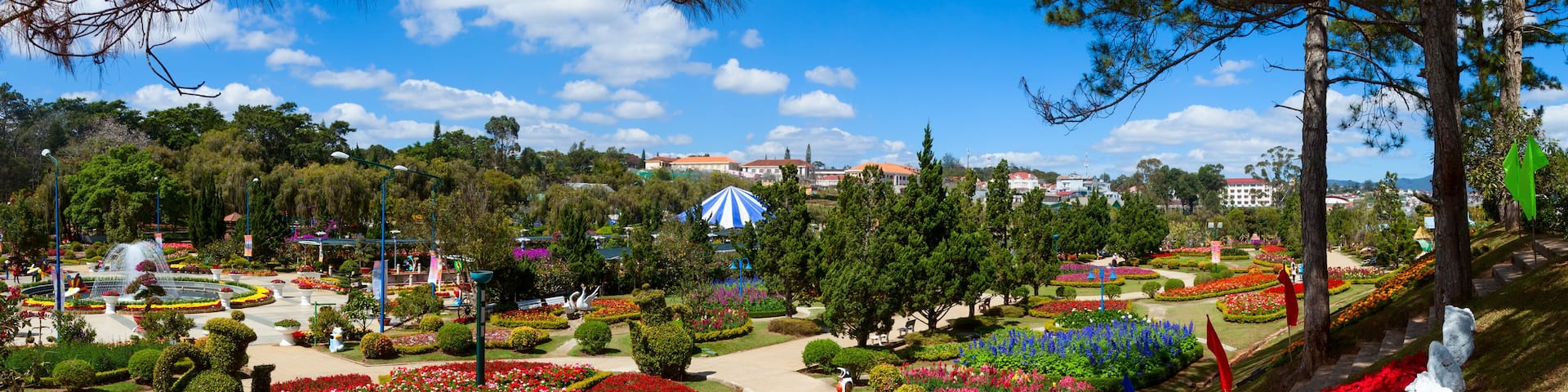 A landscaped garden with a central circular pathway, vibrant flower beds, and a distant building.