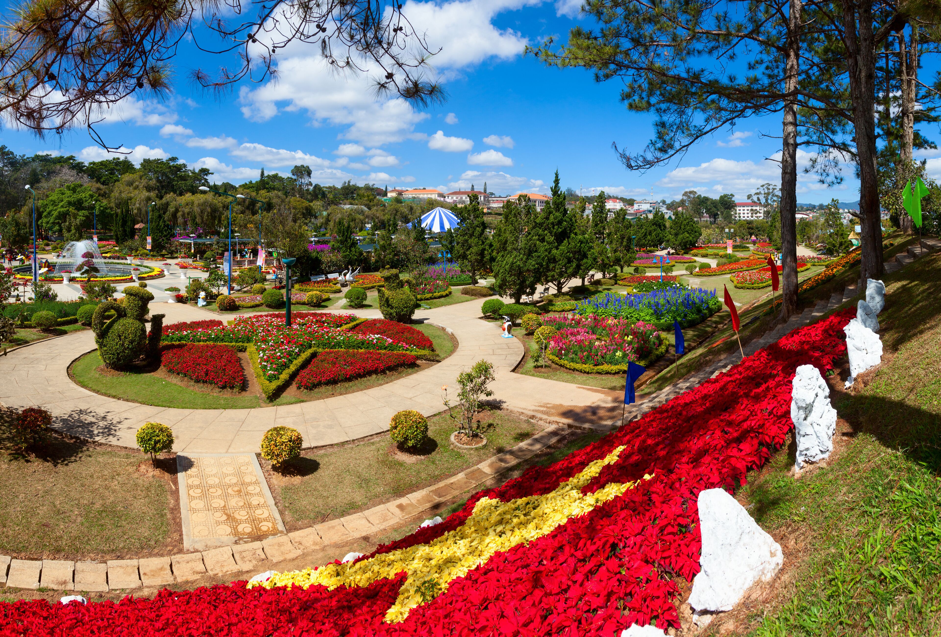 A landscaped garden with a central circular pathway, vibrant flower beds, and a distant building.