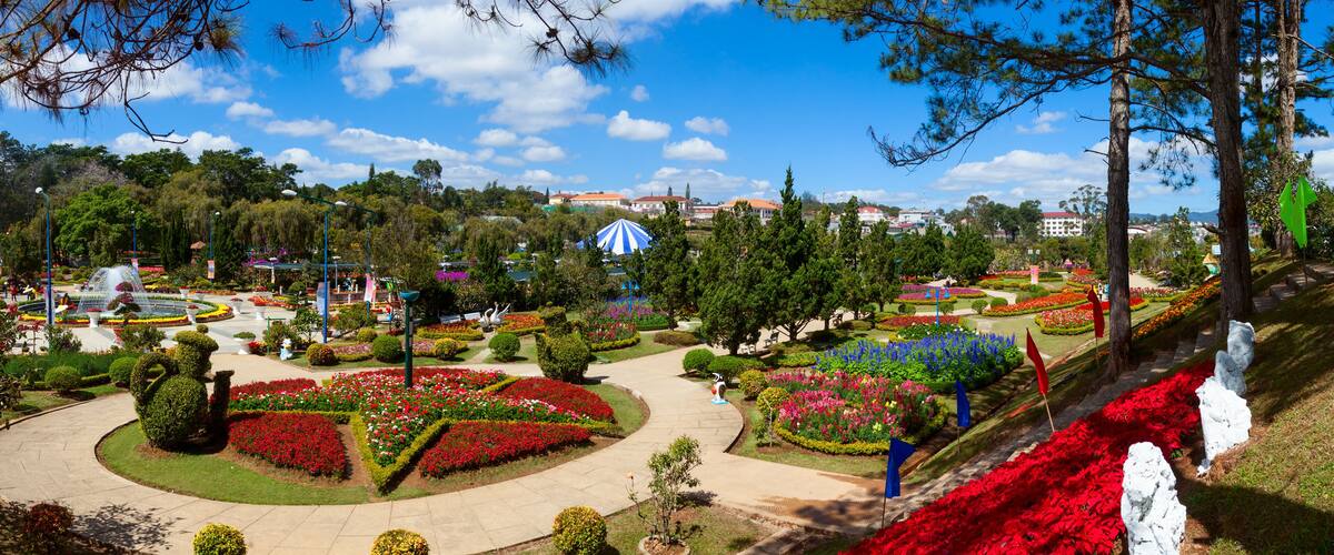 A landscaped garden with a central circular pathway, vibrant flower beds, and a distant building.
