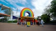A colorful rainbow archway at a park entrance with a signboard and people standing nearby.