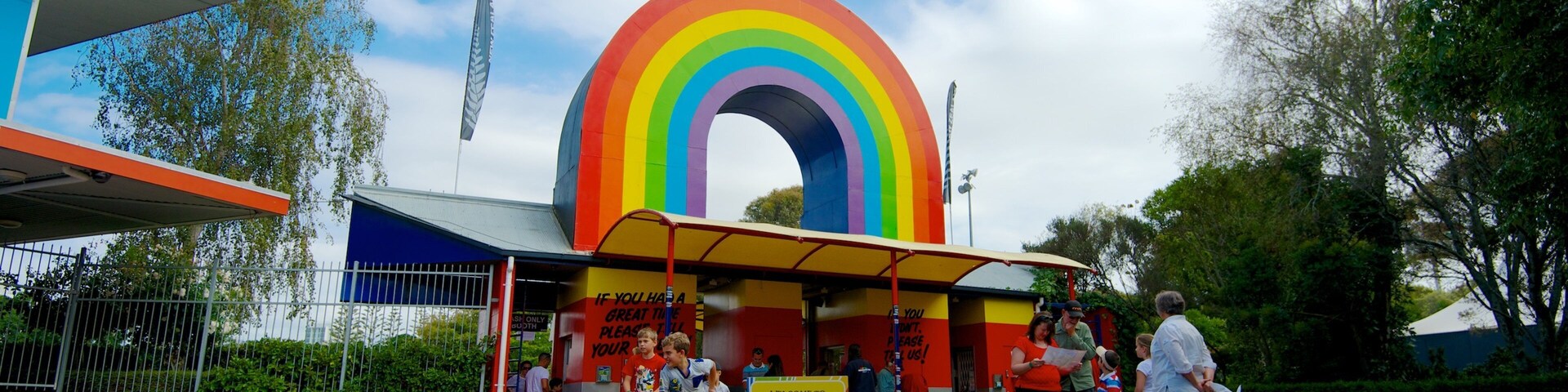 A colorful rainbow archway at a park entrance with a signboard and people standing nearby.