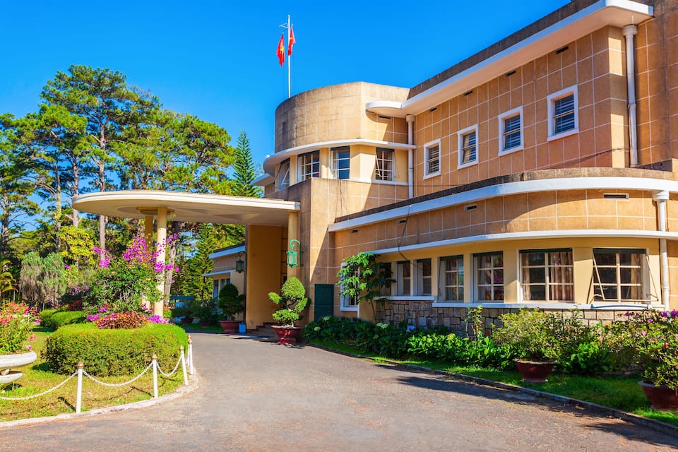 A historic building with a curved facade, a flagpole, and a well-maintained garden with various plants and flowers.