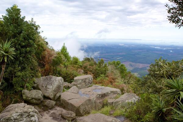 A mountainous landscape with dense vegetation, large rocks, and a distant view of a valley.