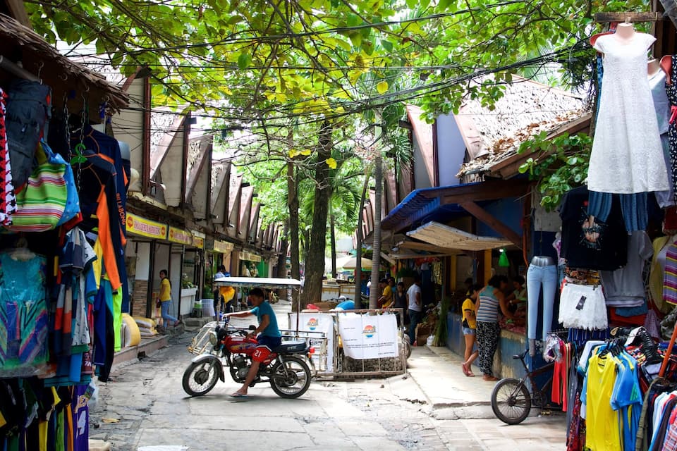 A narrow street with colorful clothing stalls and a motorcycle in the center.