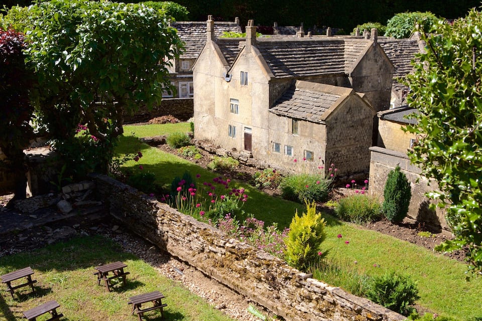 A stone building with multiple chimneys, surrounded by a well-maintained garden with flowers and a stone wall.