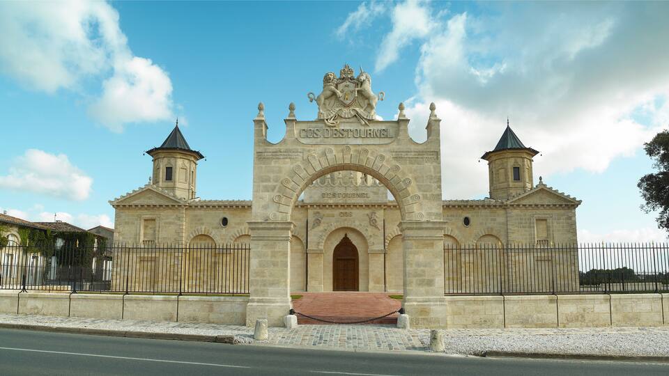 A historic stone gate with a lion statue, two towers, and the inscription "COS DESPOSTOR".