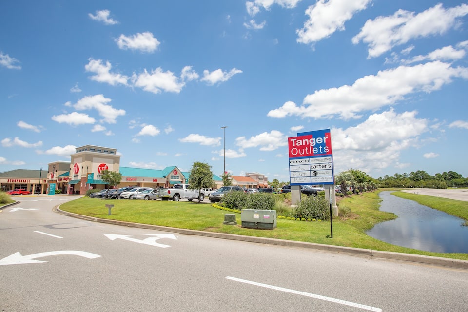 Un centro comercial con el letrero de Tanger Outlets, un estacionamiento y una pequeña fuente.