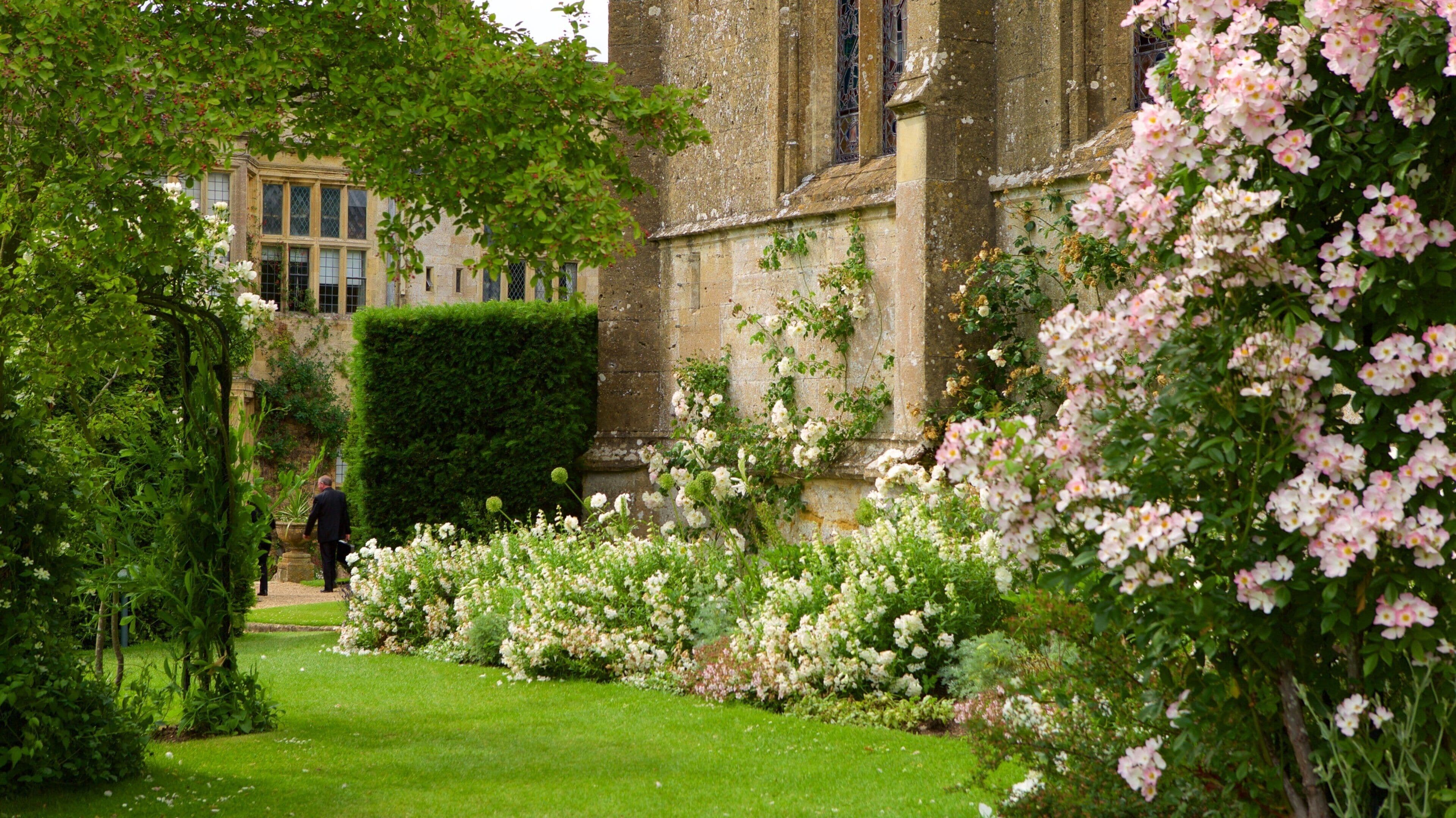 A lush garden with flowering plants and a historic building in the background.