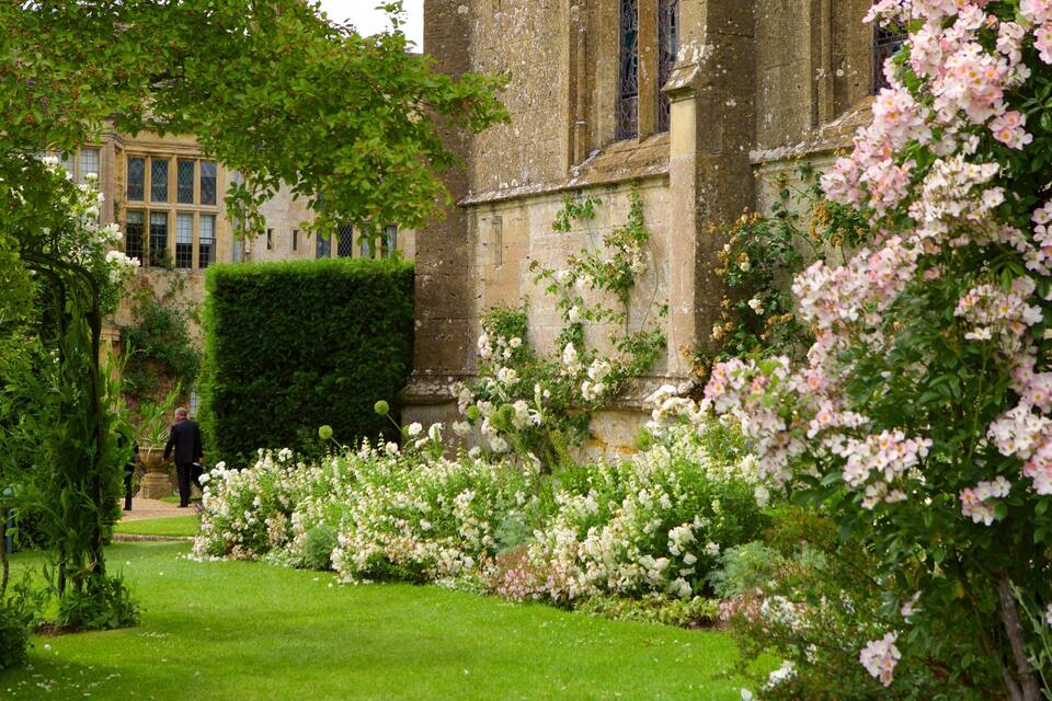 A lush garden with flowering plants and a historic building in the background.