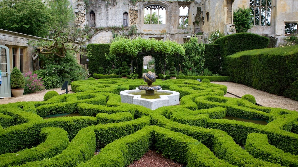 A formal garden with a central fountain, trimmed hedges, and an old stone building in the background.